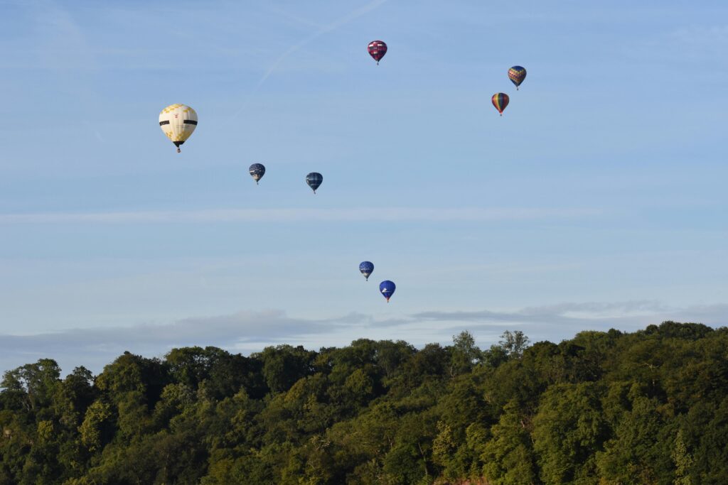 Vibrant hot air balloons drift over lush green hills in Bristol, England, on a sunny day.